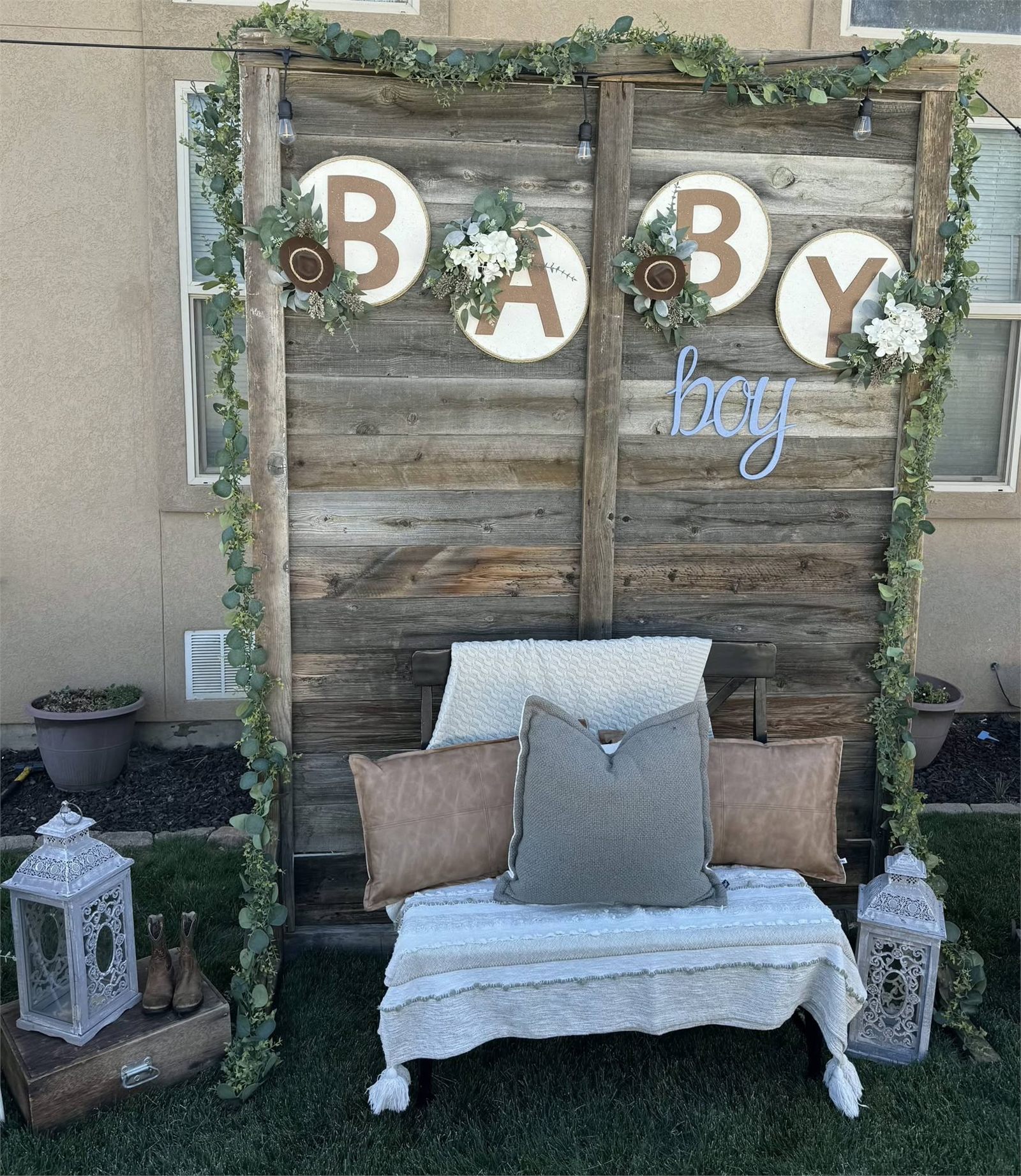 Rustic baby boy shower lounge with barnwood backdrop, eucalyptus garland, lanterns and cushions