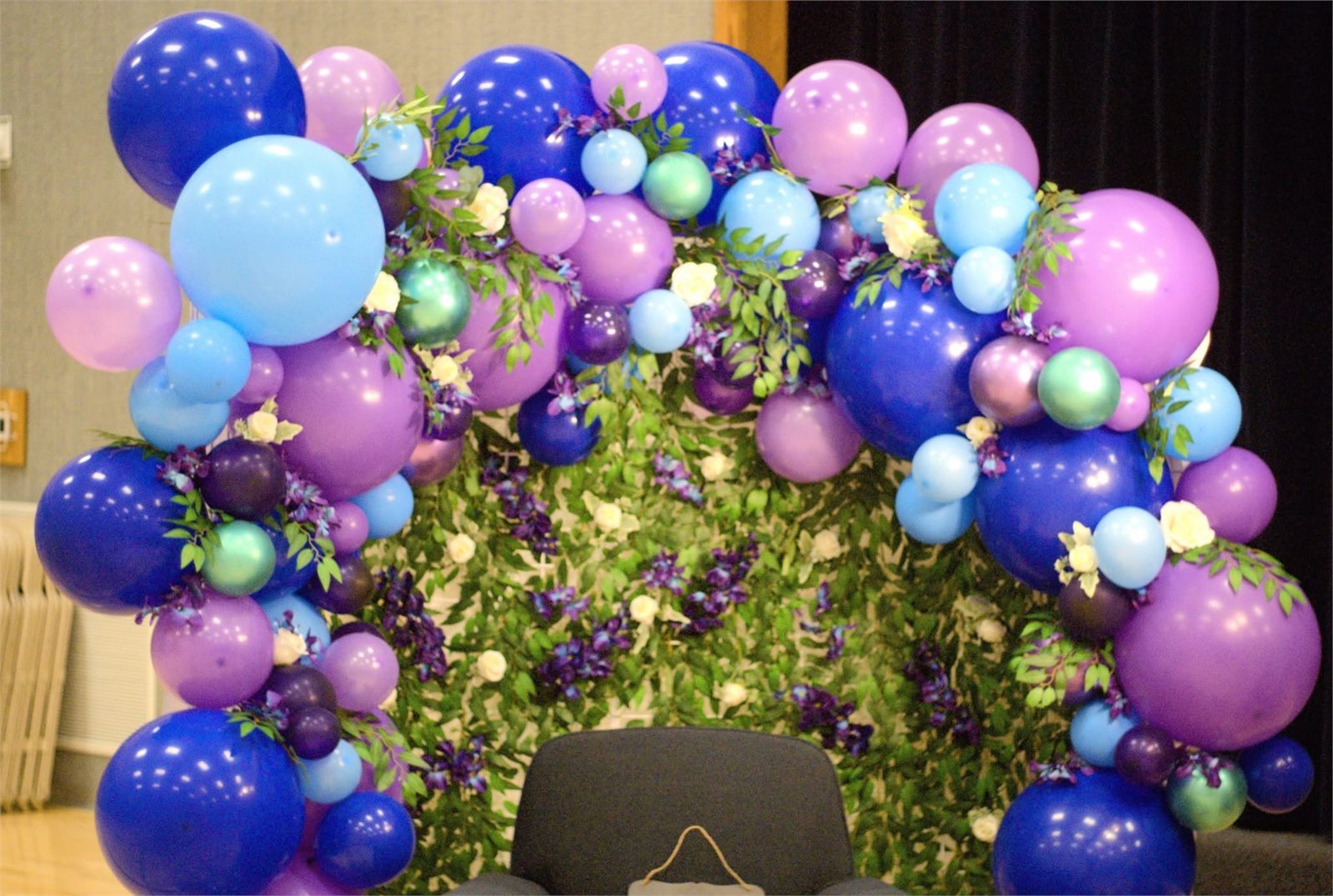 Purple and blue organic balloon arch framing a greenery flower wall