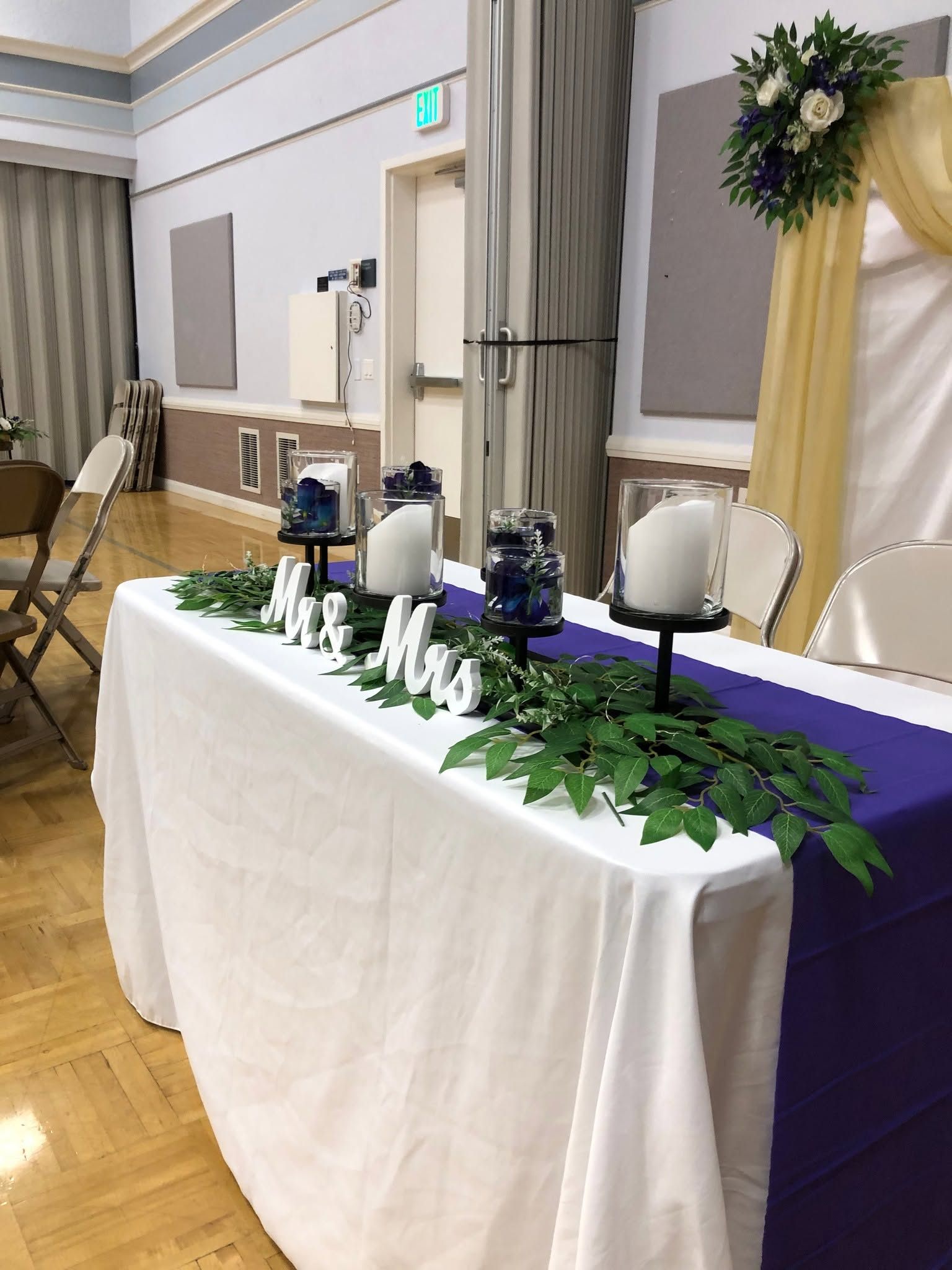 A wedding head table styled with greenery and candles