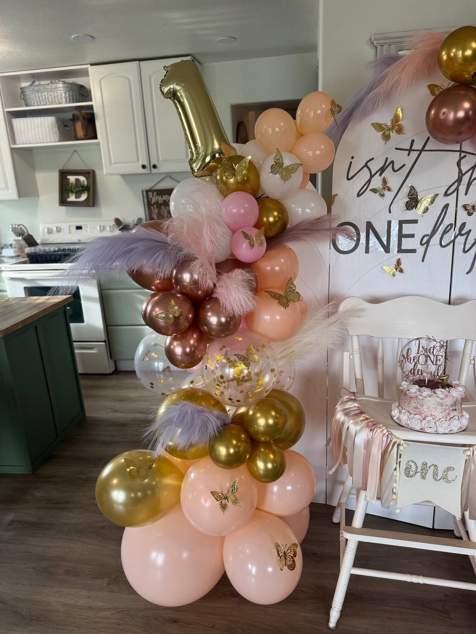 Close detail of a blush and gold balloon garland with butterflies and pampas plumes