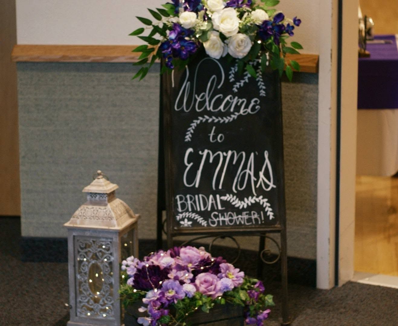 Hand lettered chalkboard welcome sign for a bridal shower with floral swag and lantern
